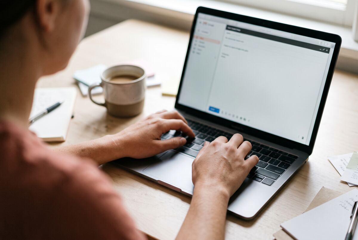Hands on a laptop with a short email on screen, a coffee beside it